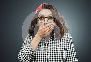 Astonished woman covers her mouth over dark gray - black background. Surprised girl. Unbelievable concept