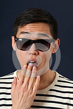 Astonished young Asian man in sunglasses covering his mouth by p