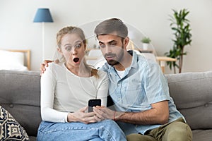 Astonished young couple surprised by internet app looking at phone