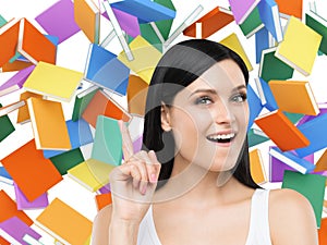 Astonishing girl is thinking about education and pointing out her finger up. Colourful books on the background.