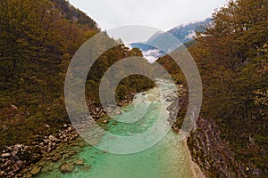 Astonishing landscape view of alpine Soca River. Emerald green water flows between mountains with dense forest.