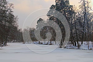 Astonishing winter landscape of frozen pond in the forest. Evergreen wood and shore in snow.
