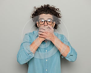 astounded casual man with curly hair covering mouth and being shocked