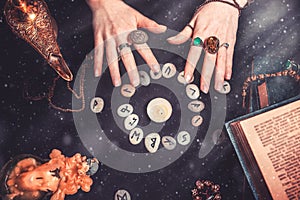 Astrology and esotericism. Female witch hands conjure over the rune circle. On a black background lie fortune-telling runes, a photo