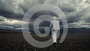 Astronaut explores an unknown red planet. Cloudy sky and mountains in the background