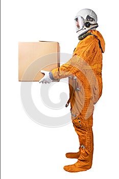 Astronaut wearing orange space suit and space helmet holding in hand brown cardboard box isolated on a white background