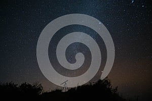 Astronomical telescope atop a hill, with the Milky Way galaxy illuminated in the background