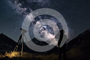 astrophotographer, with camera and tripod, capturing starry night sky above mountain range