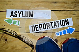 Asylum or Deportation opposite direction signs with sneakers and eyeglasses on wooden photo