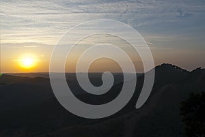 Atardecer entre montaÃ±as, cielo azul y nubes, sol brillante photo