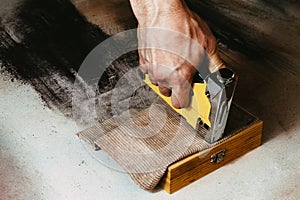 An atelier working for covering a wooden box with velvet by using a metal handtacker, stapler - on the dusty workbench, closeup