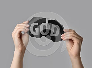 Atheism as religious position. Woman ripping black paper with word God on light grey background, closeup