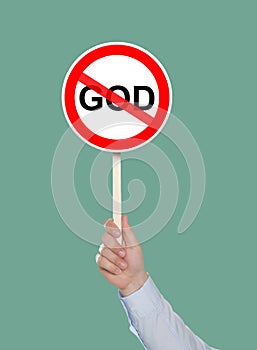 Atheism concept. Man holding prohibition sign with crossed out word God on pale green background