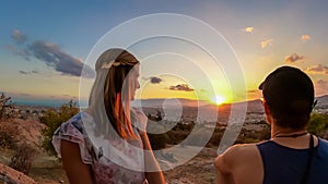 Athens - Young couple  watching sunset over city of Athens seen from Filopappou Hill (hill of muses), Athens, Greece