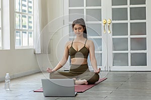 Athlete Asian indian woman looking laptop practice yoga lotus pose online course at home