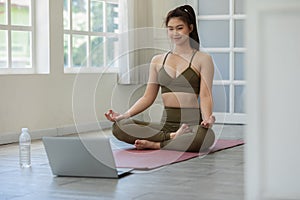 Athlete Asian indian woman looking laptop practice yoga lotus pose online course at home