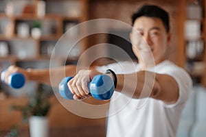 Athlete asian man doing hands exercise with dumbbells in living room interior, doing strength workout at home