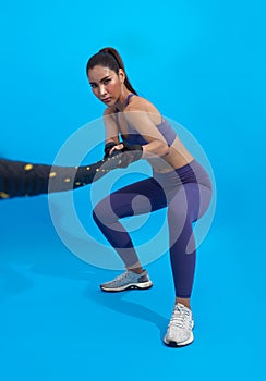 Athlete asian sportswoman pull the ropes as part of fat burning workout in fitness studio blue background. Woman exercising with