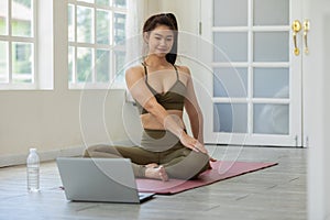 Athlete Asian woman looking laptop practice yoga online course at home to meditation comfortable and relax