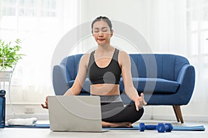 Athlete Asian young woman looking laptop practice yoga lotus pose online course at home to meditation comfortable and relax.yoga
