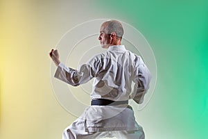 Athlete with a black belt training formal exercises against a colored background with yellow and green tints