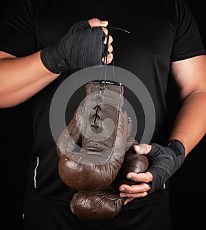 athlete in black clothes holds very old vintage leather brown boxing gloves
