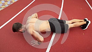 Athlete in black shorts, shirtless doing push ups on race track stadium outdoors