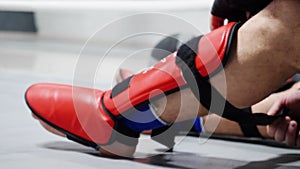 Athlete boxer man fighter in sportswear tying bandage shield on legs before boxing. Fighter wearing red leg shield