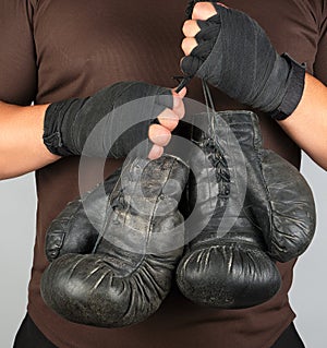 athlete in brown clothes holds very old vintage leather boxing gloves