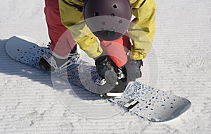 The athlete checks fastenings on a snowboard before descent.