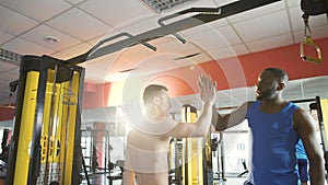 Athlete doing chin-ups, friend supporting and motivating him, giving high five