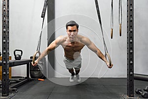 Athlete exercising on gymnastic rings in a well-equipped, modern gym. The man displays strength and determination, his muscles