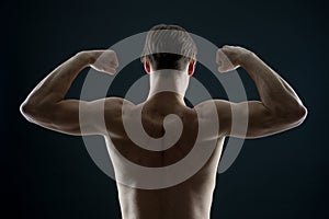 Athlete with fit torso, back view. Man bodybuilder flex arm muscles. Sportsman show biceps and triceps. Workout and training activ