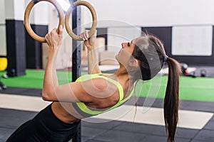 Athlete fit woman exercising in gym pulling up on gymnastic rings side view.