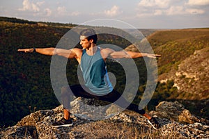 Athlete, fit, young man doing stretching exercises, workout outside on forest, mountain background. Summer landscape.