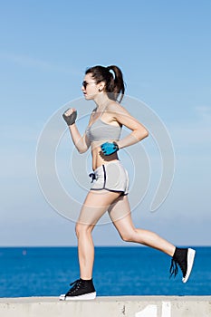 Athlete girl in gray top and shorts running alonge seafront