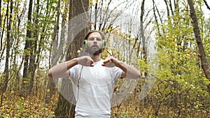 Athlete with green headphones listens to music in the park and warms up before running. Sports and health