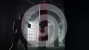 Athlete hitting punching bag in gloves. Man working out blows on sports bag