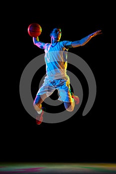 Athlete in jump pass in basketball, illuminated by colorful lighting. against black studio background in mixed neon