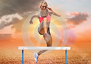 Athlete jumping over hurdles against sky in background