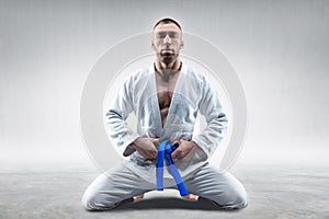 Athlete in a kimono with a blue belt sits and waits for the opponent. Concept of karate, sambo, jujitsu