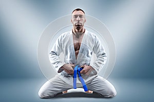 Athlete in a kimono with a blue belt sits and waits for the opponent. Concept of karate, sambo, jujitsu photo