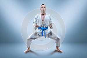 Athlete in a kimono with a blue belt stands in a fighting position. Concept of karate, sambo, jujitsu