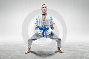 Athlete in a kimono with a blue belt stands in a fighting position. Concept of karate, sambo, jujitsu photo