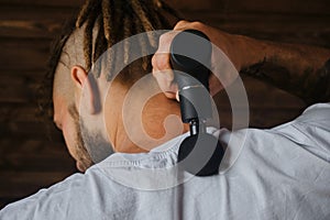 Athlete kneads neck and back muscles after training, rear view. The concept of healthy lifestyle. Caucasian man with dreadlocks