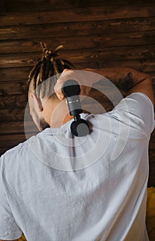 Athlete kneads neck and back muscles after training, rear view. The concept of healthy lifestyle. Caucasian man with dreadlocks