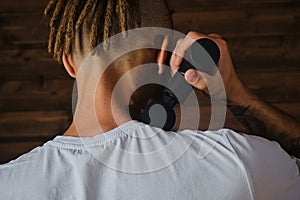 Athlete kneads neck and back muscles after training, rear view. The concept of healthy lifestyle. Caucasian man with dreadlocks