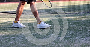 Athlete legs on tennis court holds racket and knocks ball on court