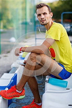 Athlete listens music with phone in his hand at stadium