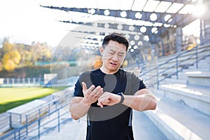 Athlete looks at watch Asian man disappointed with his result running time and calories burned after training and running